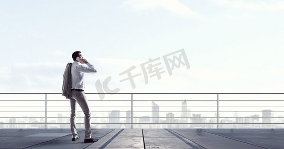 他在谈生意。男子老板有手机交谈，而站在楼顶