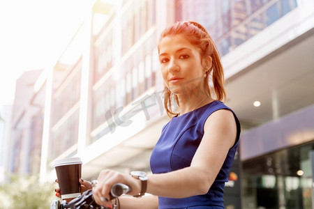 骑自行车上下班的年轻女子。穿着公务服的年轻女子骑着自行车喝着咖啡