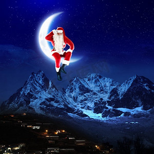 圣诞老人坐在月球上的照片。圣诞老人坐在月亮上，下面是一座城市和一座山