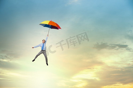 年轻的商人撑着伞在天空中高高飞翔。人撑着伞飞