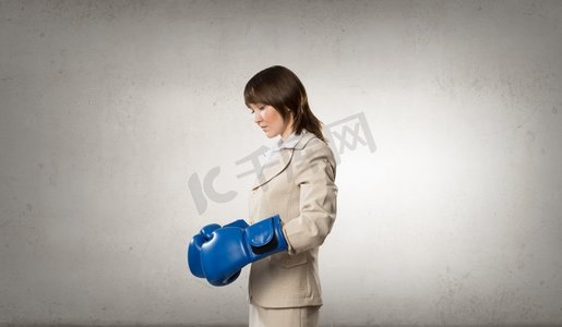 她是个斗士。年轻女商人在蓝色拳击手套比赛准备