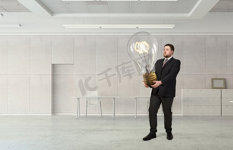 他正在实施一个想法。现代办公室里的优雅商人，手里拿着巨大的灯泡