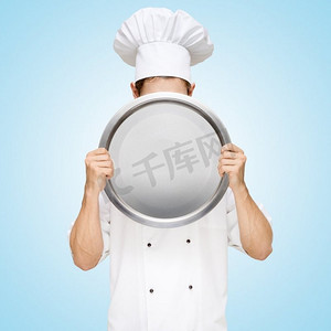 餐厅厨师躲在空盘子后面，准备一份写有价格的商务午餐菜单。