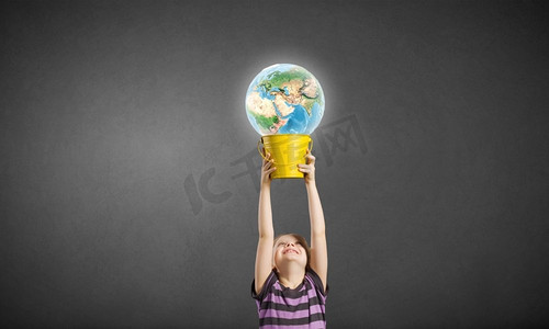 拿着水桶的孩子。可爱的女孩看着桶里的地球。这张图片的要素由美国宇航局提供