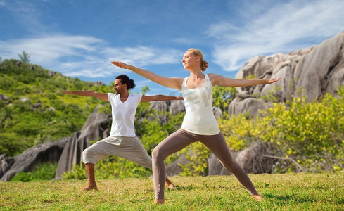 健身、运动和放松的概念-夫妻在自然背景下摆出勇士式的瑜伽。一对夫妻在海边摆出勇士的姿势做瑜伽
