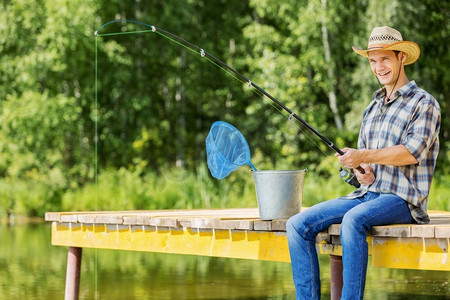 轴流式压缩机摄影照片_夏季钓鱼年轻人在帽子坐在桥和钓鱼