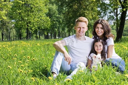 一家人在公园里。愉快的微笑的家庭画象父母和女孩坐在草与historicflowers在晴朗的夏日