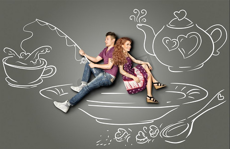 幸福的情人节爱情故事概念：一对浪漫的情侣坐在茶碟上，在茶杯里钓鱼，背景是粉笔画。