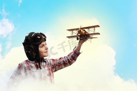 戴着飞行员头盔的小男孩在云的背景下玩玩具飞机
