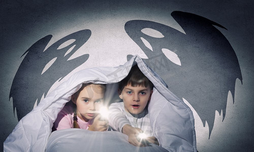 卧室黑暗摄影照片_孩子们用手电筒盖着毯子坐在床上