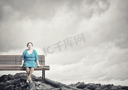 超重问题。一名身着蓝色连衣裙的中年肥胖女子坐在长凳上