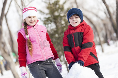 可爱的男孩和女孩在冬季公园堆雪人。冬季活动小游戏
