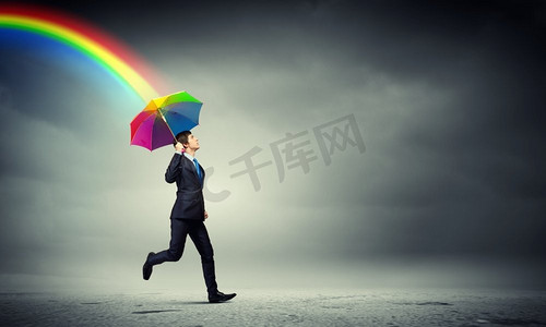 楼顶撑着伞的商人。一位穿着黑色西装、撑着雨伞的商人站在楼顶