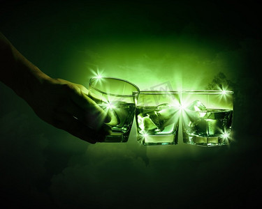 三杯加冰块的绿色苦艾酒。手拿三杯带烟的绿色苦艾酒中的一杯