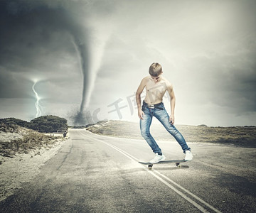 滑板上的少年。穿着牛仔裤的滑冰者在路上，背景是龙卷风