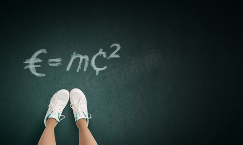 穿鞋子摄影照片_物理学中的公式。穿运动鞋的女孩站在黑板上的俯瞰