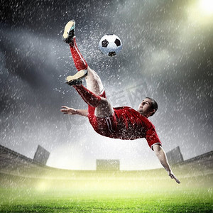 足球运动员击球。在红色衬衫的足球运动员在雨中在体育场击球