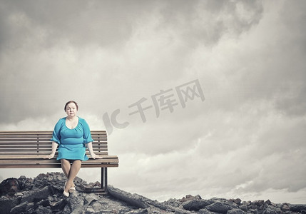 超重问题。一名身着蓝色连衣裙的中年肥胖女子坐在长凳上