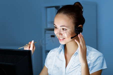 少妇在企业佩带在头戴式耳机工作与计算机