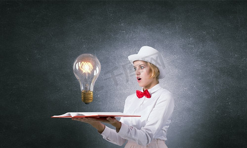 能激发你想象力的书。戴着白色帽子的年轻女子，手里拿着打开的书，书页上放着玻璃灯泡