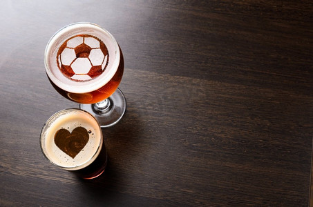 喜欢足球和啤酒。在两杯新鲜啤酒的心脏和足球剪影在酒吧桌上，从上面的看法
