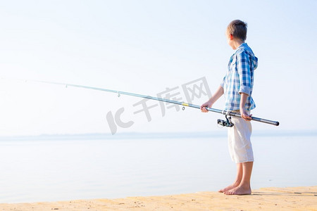 穿蓝衬衫的男孩站在馅饼上。穿着蓝色衬衫的男孩站在海边的码头上，手里拿着一根钓鱼竿