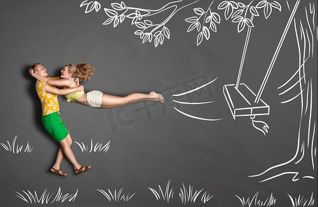 情侣浪漫背景摄影照片_快乐情人节以粉笔画为背景的浪漫情侣的爱情故事概念。一名男子看到他的女朋友从树上的秋千上跳下来。