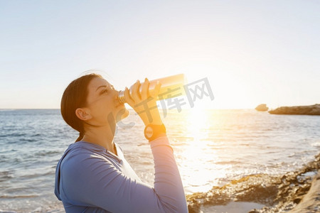 女人在海滩上喝水。年轻女子饮用水后行使在海滩上