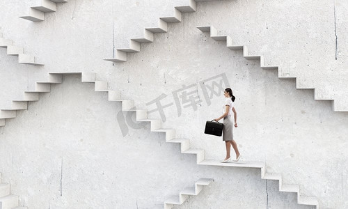 女人爬楼梯摄影照片_在事业的阶梯上。女商人与手提箱加强石头楼梯