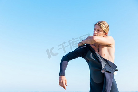 一名年轻的冲浪者在海滩上穿上潜水服。准备好乘风破浪