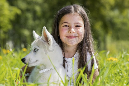 哈士奇小狗狗摄影照片_带着哈士奇小狗的小女孩。小女孩带着哈士奇小狗在夏天的草地上种着蒲公英