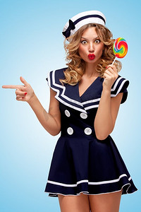 一张俏皮的水手女孩的创意照片，拿着五颜六色的棒棒糖，在蓝色背景上用手指指向一边。