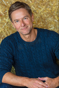 肖像拍摄的是一个有魅力、成功和快乐的中年男子，他穿着蓝色毛衣坐在谷仓或马厩的干草捆上