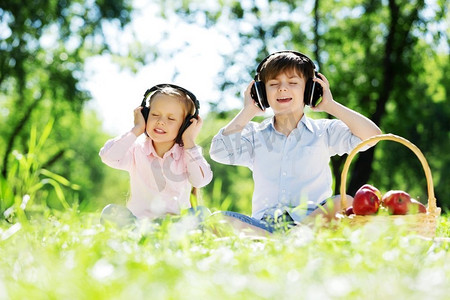 可爱的男孩和女孩在夏天公园听音乐。夏季周末
