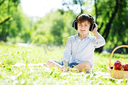 天籁摄影照片_夏日公园里戴着耳机的快乐小男孩。天籁之声