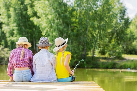 夏日休闲。后视图的三个孩子坐在银行和钓鱼