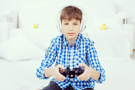 ui游戏框摄影照片_玩游戏机的男孩。情绪激动的男孩坐在地板上玩操纵杆游戏
