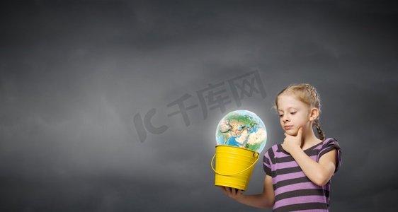 拿着水桶的孩子。可爱的女孩看着桶里的地球。这张图片的要素由美国宇航局提供