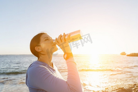 一名妇女在海滩上喝水。年轻女子在海滩上运动后喝水