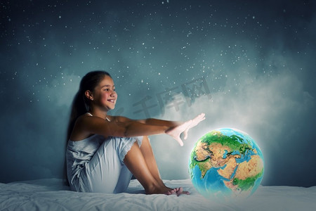 晚上做梦。可爱的女孩坐在床上，看着地球行星。这张图片的元素是由美国宇航局提供的