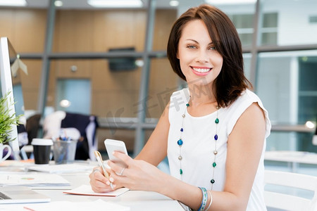 现代商务女性在办公室里拿着手机。现代成功商界女性