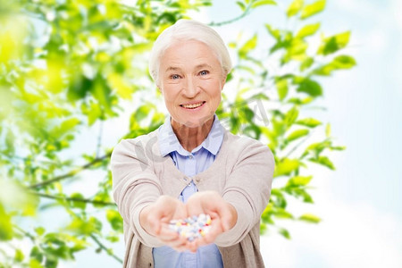 年龄，医学，医疗保健和人民的概念-快乐的老年妇女与绿色自然背景下的药片。快乐的老年妇女在家中吃药