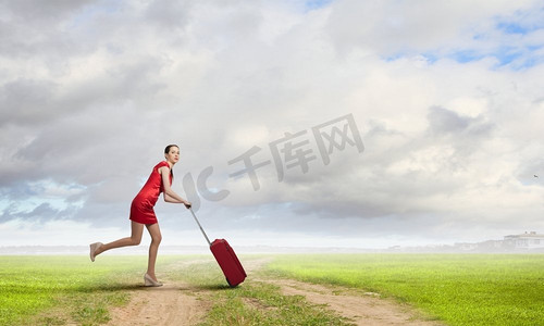 行李箱红色摄影照片_穿红衣服的女人。年轻女子穿着红色连衣裙，背着红色行李箱