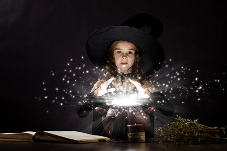 万圣节看书小孩摄影照片_万圣节女巫。小万圣节女巫在锅上读魔术