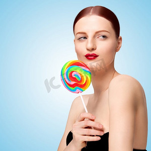 一张俏皮漂亮的女孩拿着五颜六色的棒棒糖，在蓝色背景下看着一边调情的创意照片。