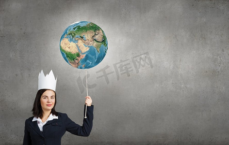世界的女王！纸皇冠的年轻女商人拿着地球行星气球。这张图片的元素是由美国宇航局提供的