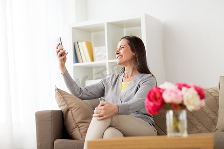 科技与人的概念--在家中自拍智能手机的快乐女性。快乐的女人在家中自拍智能手机