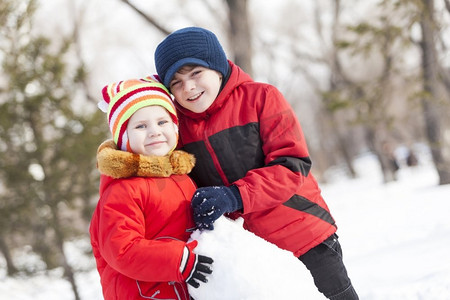 可爱的男孩和女孩在冬季公园堆雪人。冬季活动小游戏