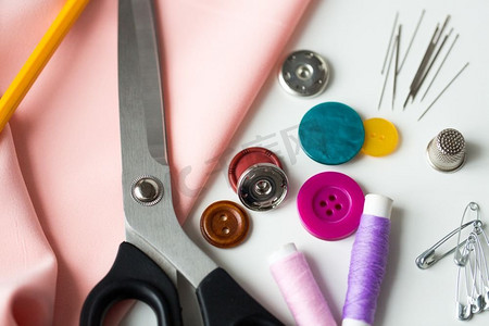 缝纫剪刀摄影照片_刺绣和裁剪概念-剪刀、缝纫纽扣、线轴、针和布。剪刀、缝纫工具和布料