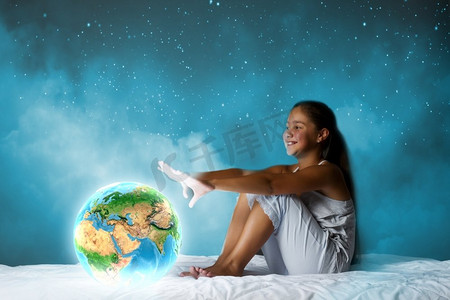 晚上做梦。可爱的女孩坐在床上，看着地球行星。这张图片的元素是由美国宇航局提供的